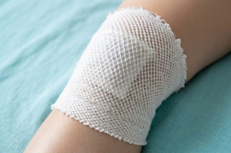 ein Knie mit einem Verband und einer Kompresse in weiß